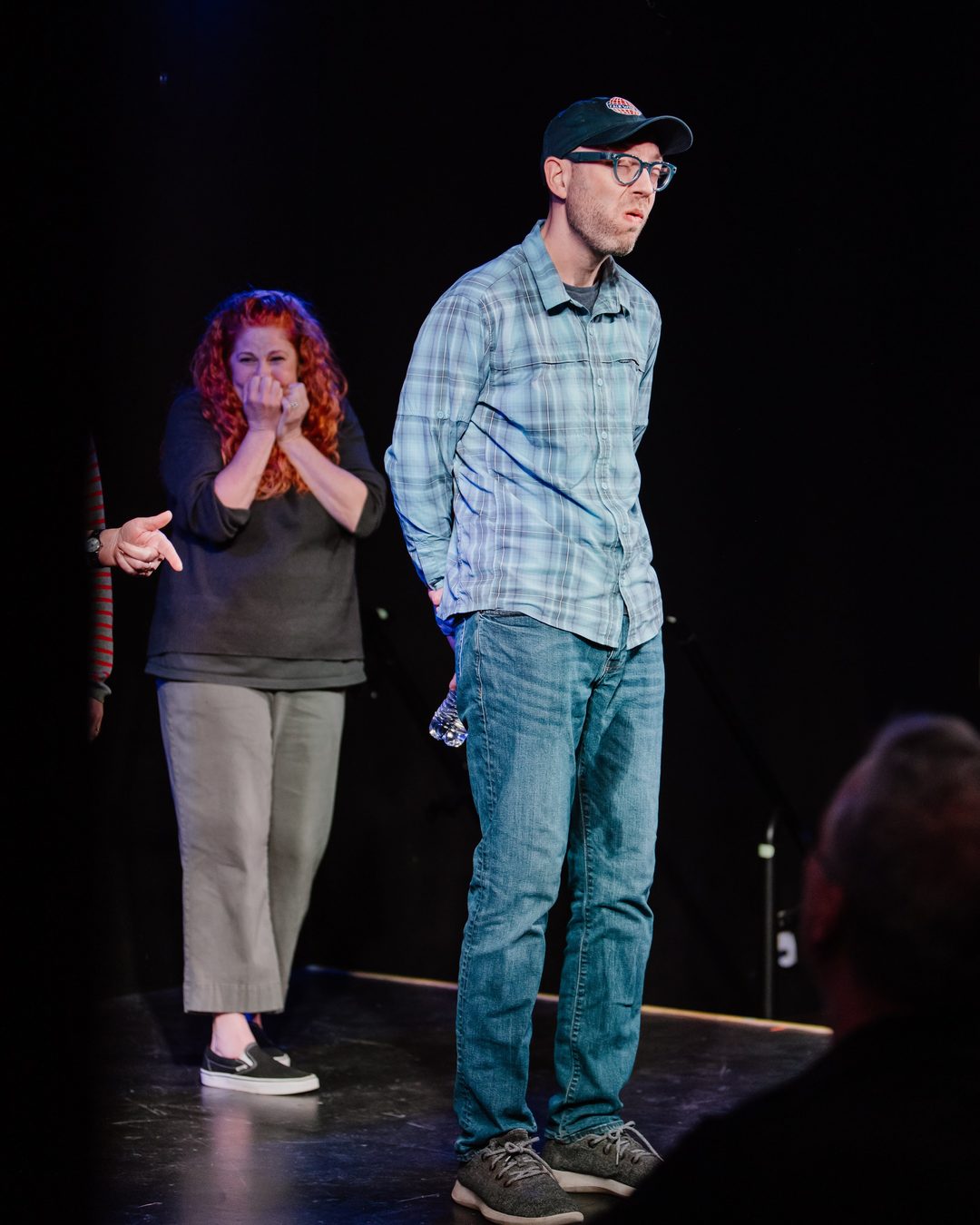 Erik standing on stage with the water bottle as a castmate covers her face